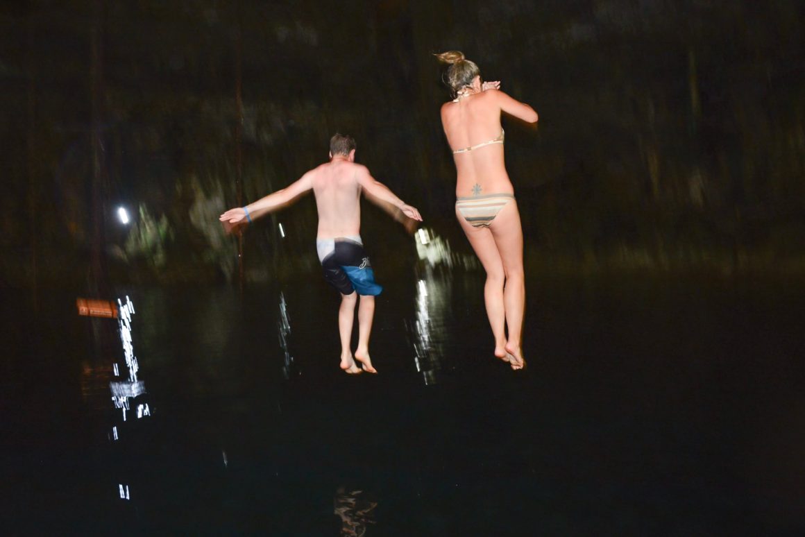 girl and boy (Christina and Jamie) jumping into Cenote Maya in Riviera Maya, Mexico